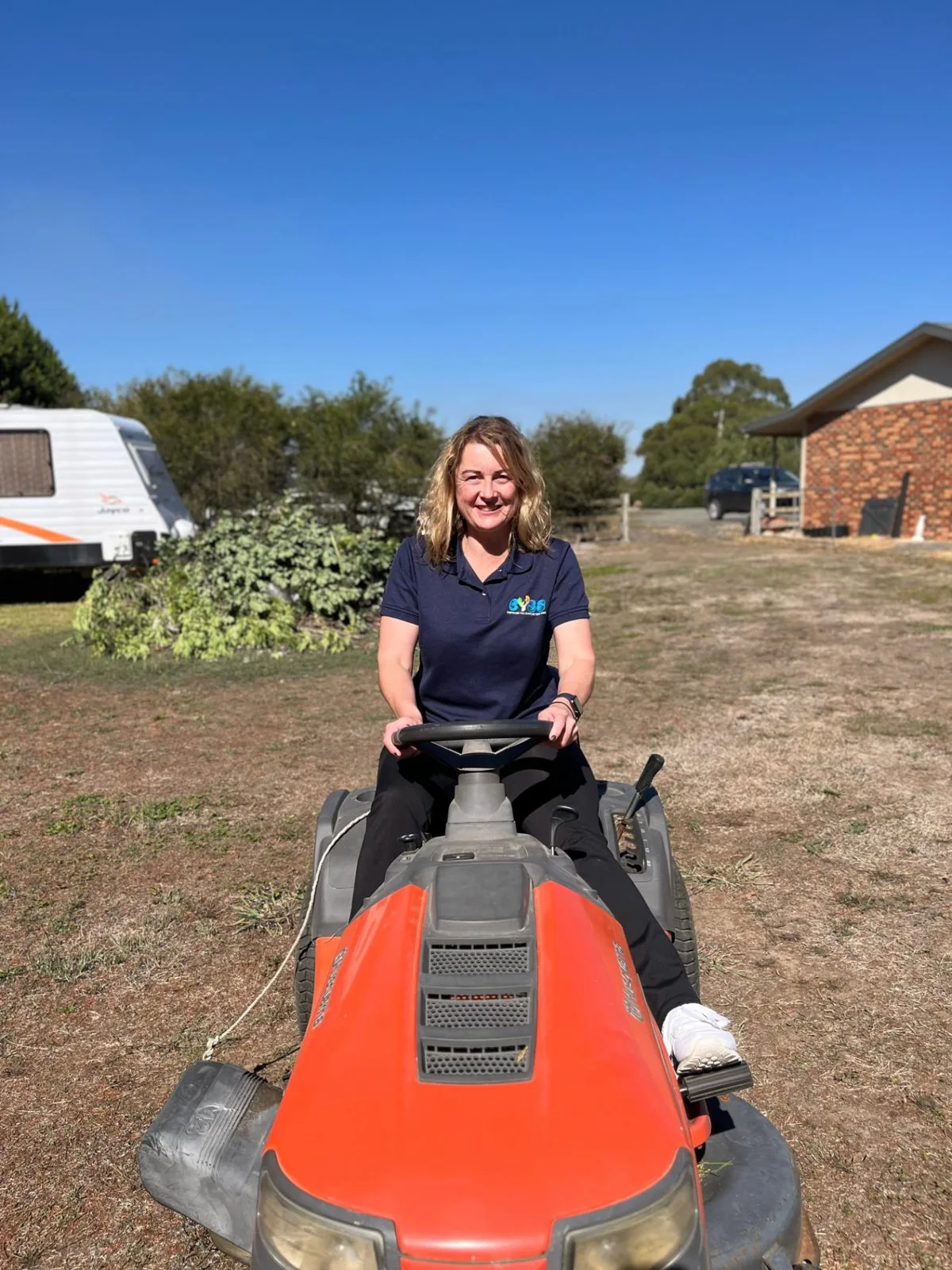 EYSS support worker mowing a country yard under a clear blue sky