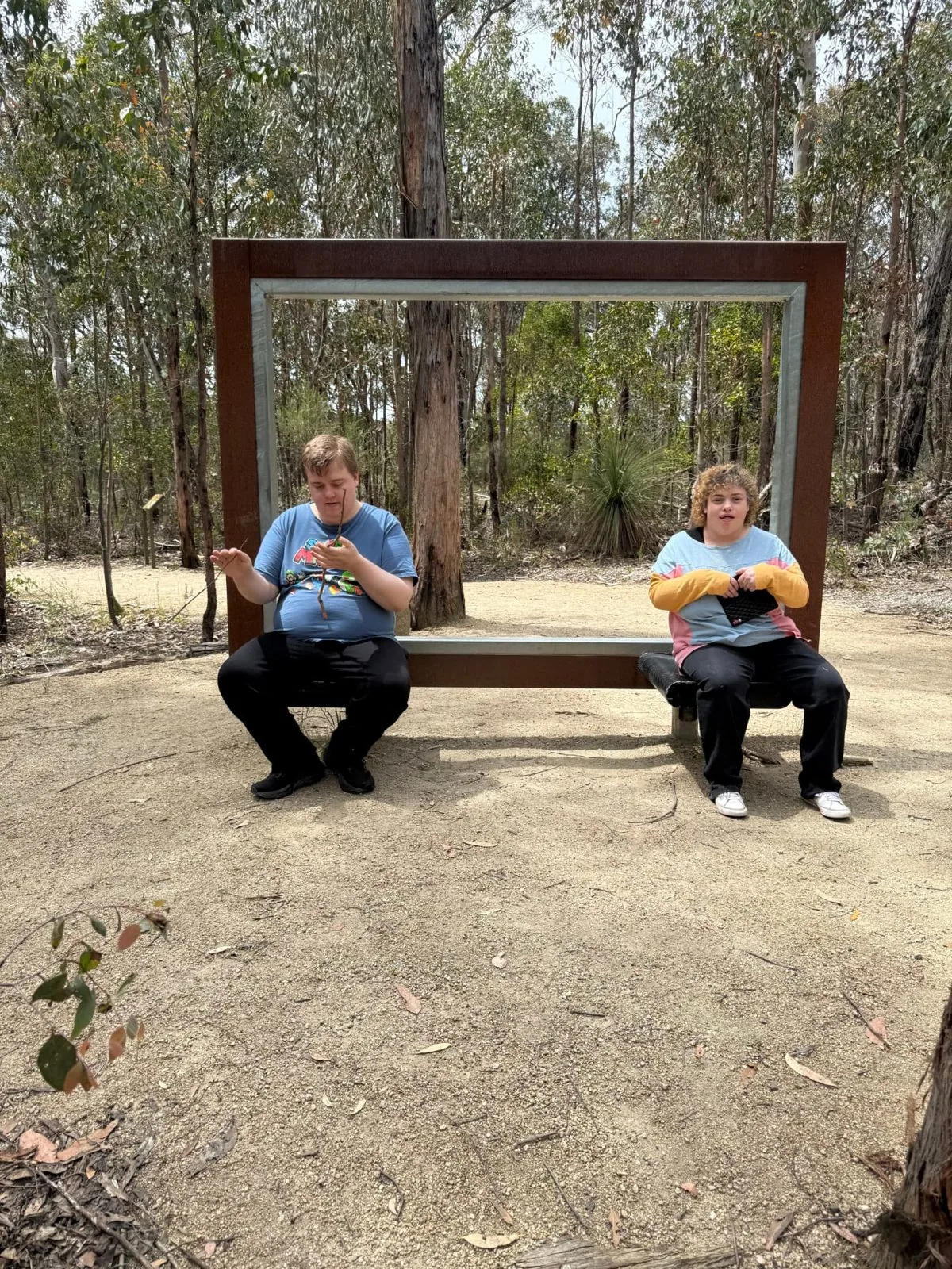 Two participants sitting by a picture frame sculpture in the bush